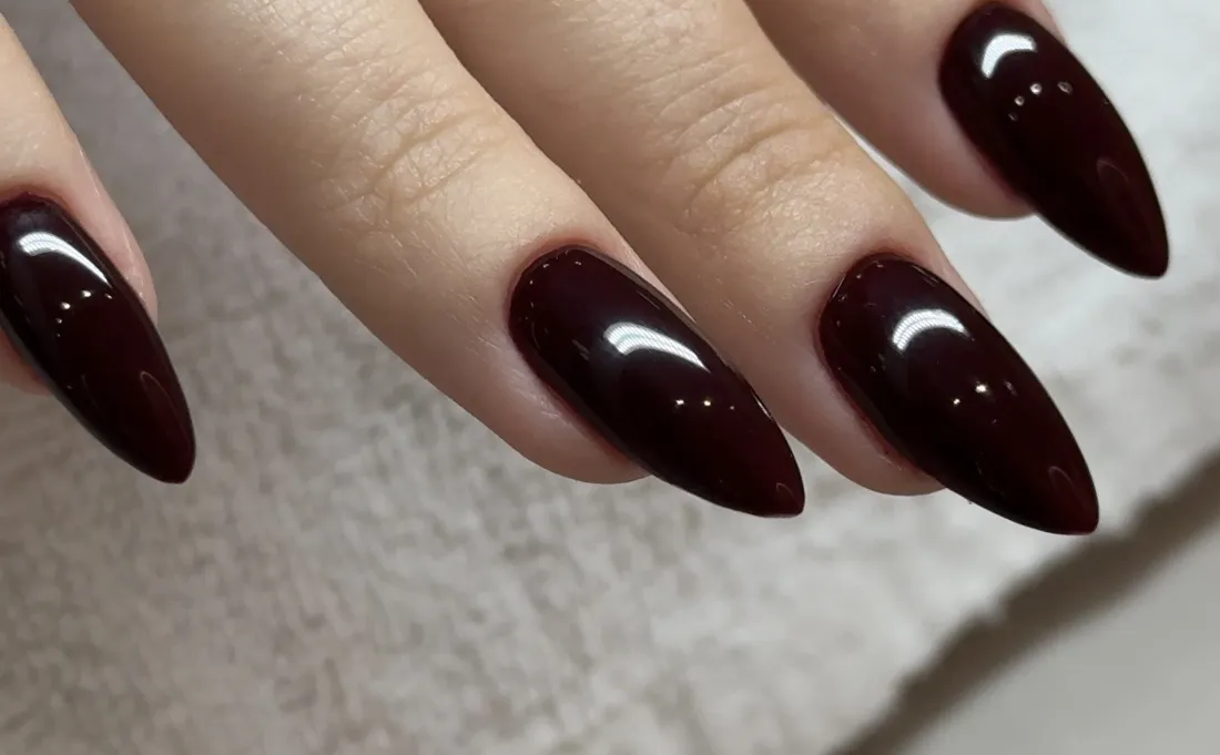 Gros plan sur des ongles amande bordeaux réalisés par Grace